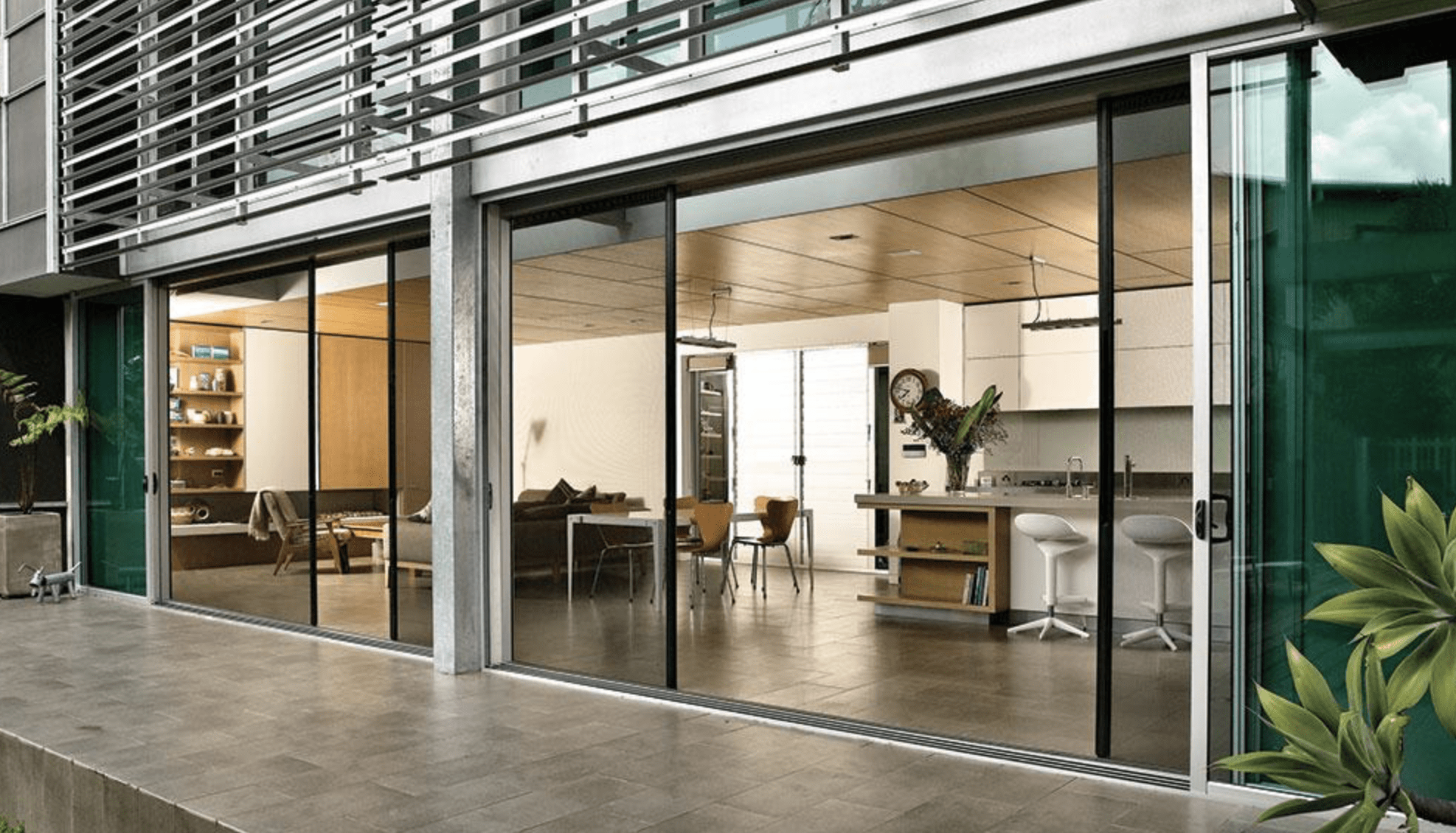 Modern open-plan living area with floor-to-ceiling sliding glass doors, showcasing a living room, kitchen, and dining space with contemporary furnishings and wooden accents.