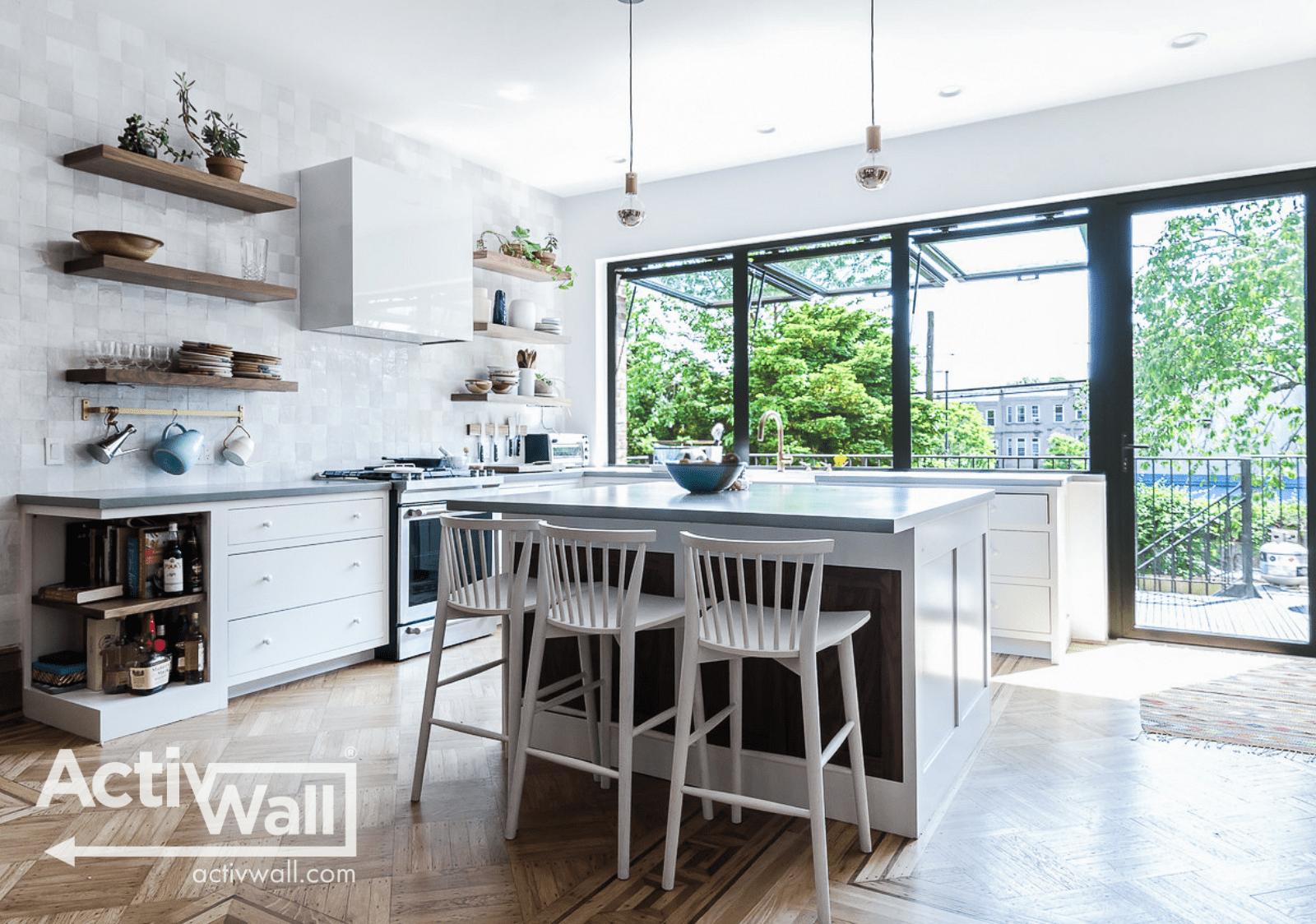 Bright and modern kitchen with an island, white cabinets, open shelves, and large windows overlooking greenery outside.