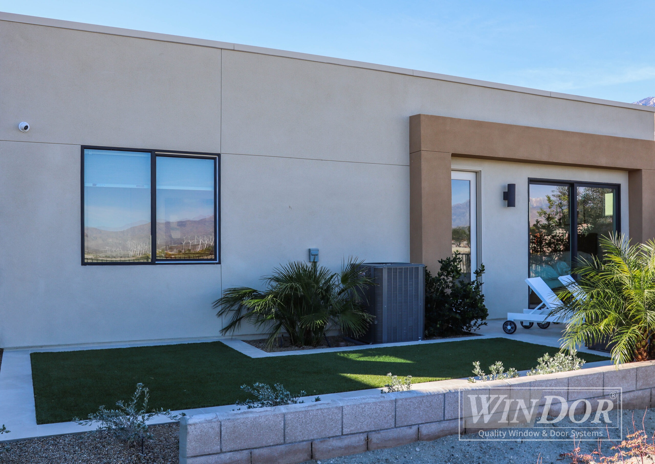 A contemporary kitchen viewed through a large open sliding glass door, with a cat lying on the ground in the foreground.